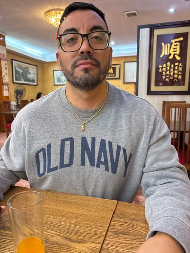 Un cliente sentado en una mesa lleva puesto el brillante Colgante Hermés Oro.
