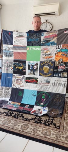 Customer holding up a large Project Repat T-Shirt Quilt composed of various colorful t-shirt squares.