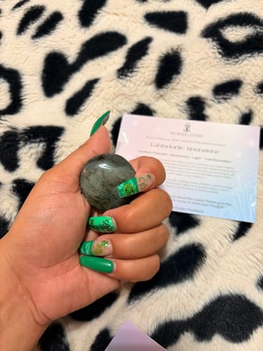 Reviewer's hand holding a round, polished Labradorite Moonstone crystal with the product description card in the background.