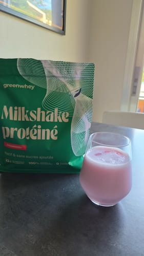 Avis d'un client : le sachet vert du Milkshake protéiné à la fraise à côté d'un verre de la boisson rose préparée.