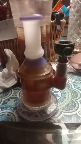 Reviewer's colorful glass bong on a patterned surface, with the Roll Ready Ground flower visible in the bowl.
