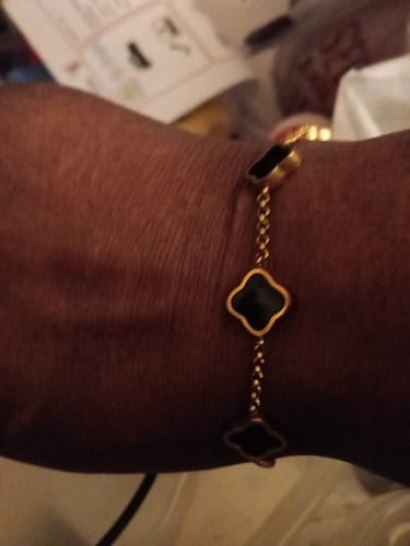 Close-up of a customer's wrist wearing a gold-colored chain bracelet with black clover-shaped charms.