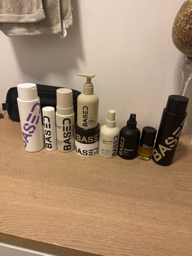 Reviewer's collection of BASED hair products, including the Hydration & Volume Duo, on a wooden counter.