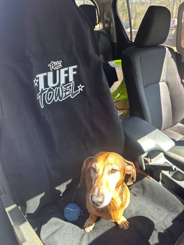 Customer's black Tuff Towel seat cover on a car seat, with a small dachshund dog sitting next to it.