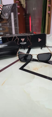 Reviewer's Velar golden and black rectangle sunglasses on a table, with the product box and case in the background.