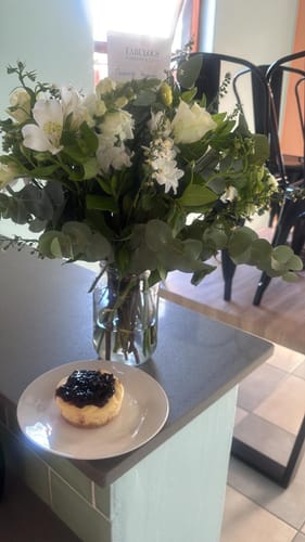 Customer's individual Blueberry Cheesecake on a plate, placed on a counter next to a vase of white flowers.