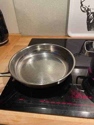 Kunde zeigt die saubere, fein gehämmerte Titanpfanne auf einem Induktionskochfeld.