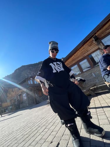 Reviewer posing outdoors in the baggy black snow pants at a sunny mountain resort.