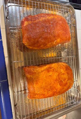 Reviewer's two pork loins covered in a red seasoning rub from The Pit Master Gift Basket, placed on a wire rack before cooking.