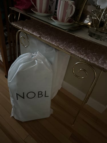 Reviewer's white Weekender Dust Cover with a drawstring top, standing on a hardwood floor.