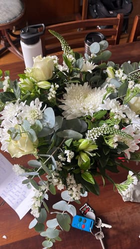 Reviewer's photo of the Peace in a Jar arrangement, a lush bouquet of white flowers and greenery on a wooden table.