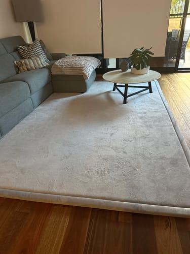 Customer's soft, light grey Mellow Mat placed in a living room on a wooden floor.