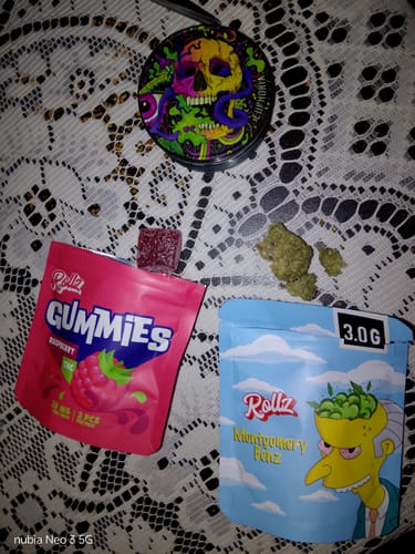 Customer's pink pouch of ROLLZ THC gummies with one gummy shown next to other cannabis products on a lace surface.