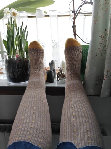 Anmelderens fødder i beige Støttestrømper med gule tæer og prikker, mens de slapper af ved et vindue.