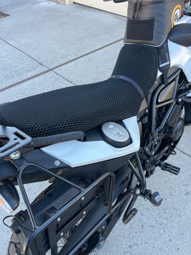 Customer's black mesh Wind Rider Seat Cover installed on a white and black motorcycle, seen from the side.