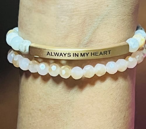 Close-up of a reviewer's wrist wearing two stacked bracelets, including the engraved 'ALWAYS IN MY HEART' bracelet.