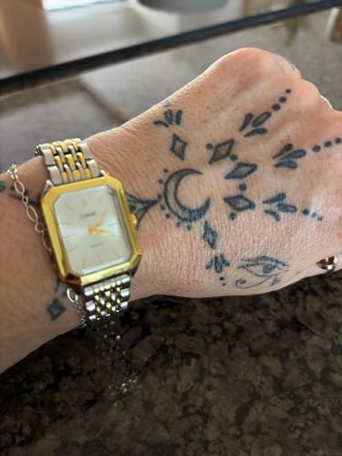 A reviewer's CLAIRE DE MAINS watch with a two-tone band and rectangular face, worn on their wrist.