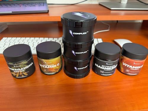 A reviewer's collection of various Complex brand supplements arranged on a wooden desk.