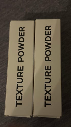 Reviewer shows two boxes of Texture Powder standing side-by-side.
