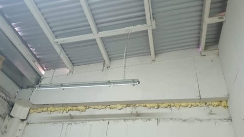 Cliente muestra la Espuma de Poliuretano amarilla aplicada para sellar la junta entre la pared y el techo en un entretecho.