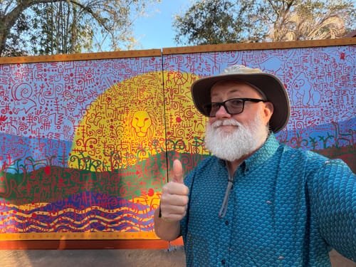 Reviewer wearing the blue Wee Cows shirt, smiling and giving a thumbs up in front of a colorful mural at a theme park.