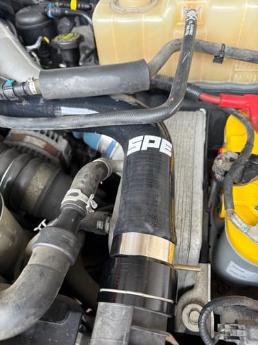 Close-up of the customer's black SPE Motorsport Upper Radiator Hose with a worm gear clamp installed in a Ford Powerstroke engine.