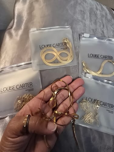 Customer's hand holding several gold-colored jewelry items from the bundle, with other pieces visible in their clear pouches.