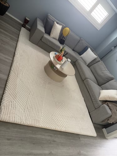 Customer's textured Mellow Mat with a vector line design in a living room next to a grey sectional sofa.