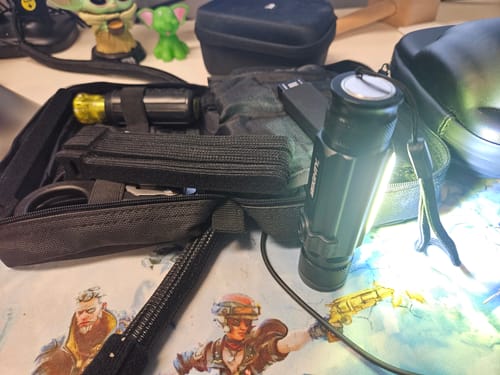 Customer's black 80Eighty® Flashlight with its bright side light on, sitting next to a black utility pouch.