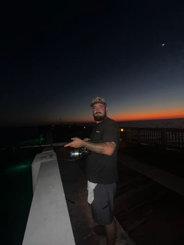 Customer wearing the Hat of the Month while fishing on a pier at dusk.