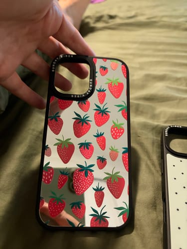 Customer holding the Berry Cheeky iPhone Case, showing its reflective mirrored surface and strawberry pattern.