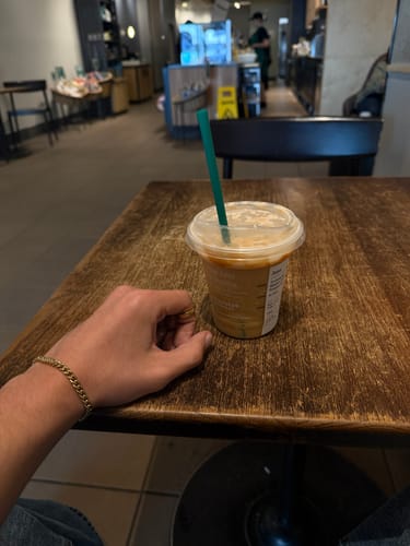 Customer's hand resting on a wooden table, wearing the gold 5mm Cuban Link Bracelet on their wrist.
