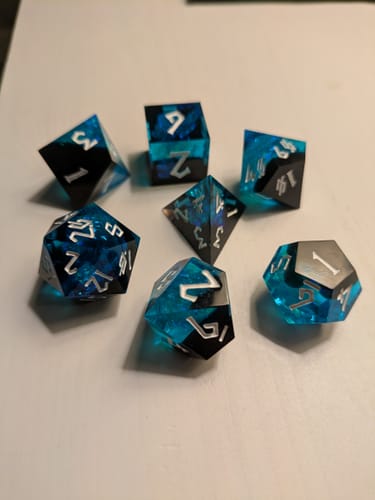Reviewer's Moonbeam Sharp-Edged Resin Dice Set in gorgeous blue and black resin with reflective bits inside.