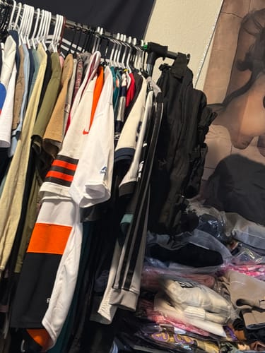 Customer's various wholesale sports jerseys hanging on a packed clothing rack and piled below.