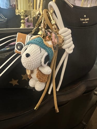 Reviewer's EVIL EYE STACK CHARM with a crochet dog and camera charm attached to the strap of a black bag.