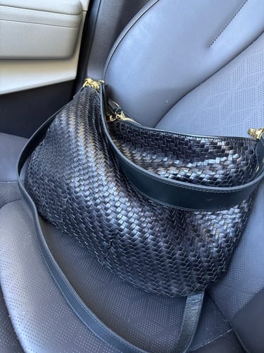 Reviewer's black woven Moyen Messenger bag looking slouchy on a dark car seat.