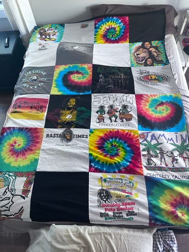 Customer's colorful Project Repat T-Shirt Quilt made from reggae-themed and tie-dye shirts, spread across a bed.