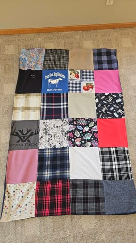 Customer's completed Premium T Shirt Quilt, made from a patchwork of colorful shirts, laid on a floor.