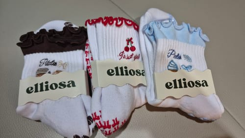 Reviewer's three pairs of white Pilates & Chill socks, each with a unique ruffled cuff design in brown, red, and blue.