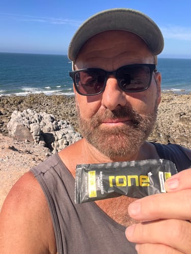Reviewer holds a packet of SuperCharged Honey while standing on a rocky coast.