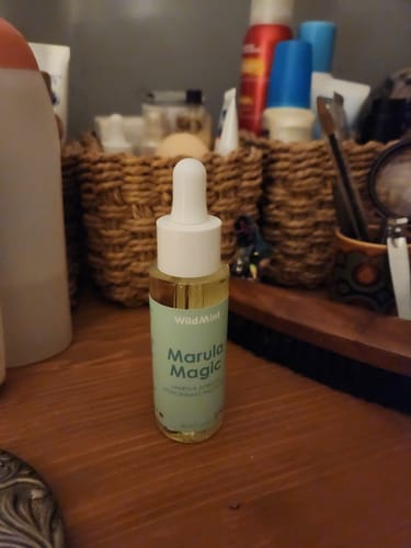 Reviewer's bottle of Marula Magic facial oil on a wooden counter with other toiletries in the background.
