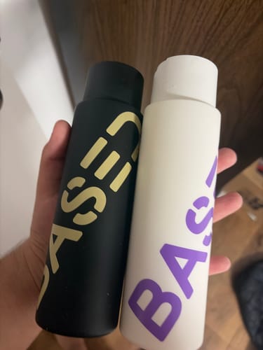 Customer holding two BASED bottles, the conditioner and shampoo. One bottle is white and the other is black.