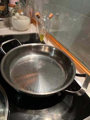 Ein Kunde zeigt die saubere, fein gehämmerte Titanpfanne mit zwei Griffen auf einem Kochfeld.