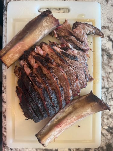 Customer's cooked Bone-In Short Ribs, sliced to show a dark crust, next to the bones on a cutting board.