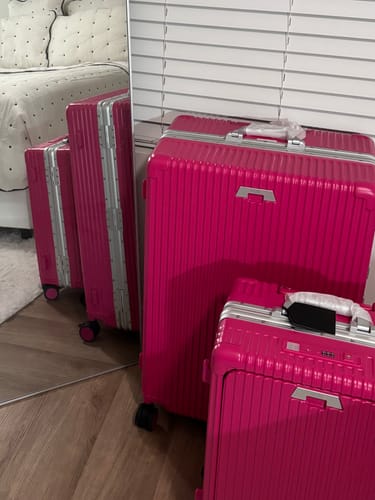 Reviewer's vibrant pink All-in-One Carry-On and matching larger suitcase, shown together in a bedroom.