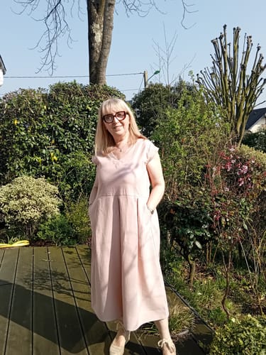 Une cliente porte la Robe Louison rose poudré en extérieur, les mains dans les poches.