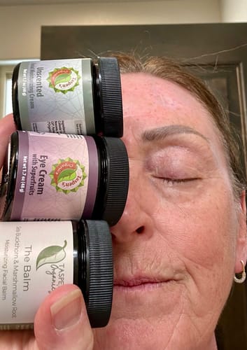 Reviewer holds jars of the Facial Moisturizing Cream and other products stacked vertically next to her face.