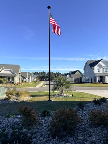 Customer's tall, black Ultra Heavy-Duty Home Flagpole installed in their front yard on a clear day.