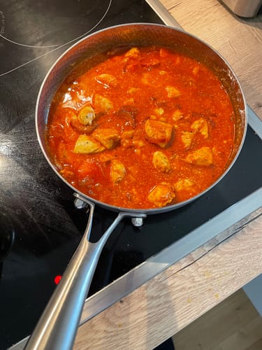 Ein Kunde kocht ein Gericht in Tomatensoße in der gehämmerten Titanpfanne auf einem Kochfeld.