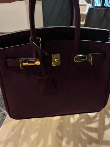 Customer holding their burgundy Warkin Bag, showing its pebbled leather and shiny gold lock hardware.